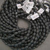 Multiple strands of matte black lava stone oval beads showcasing natural pores and charcoal-black surfaces.