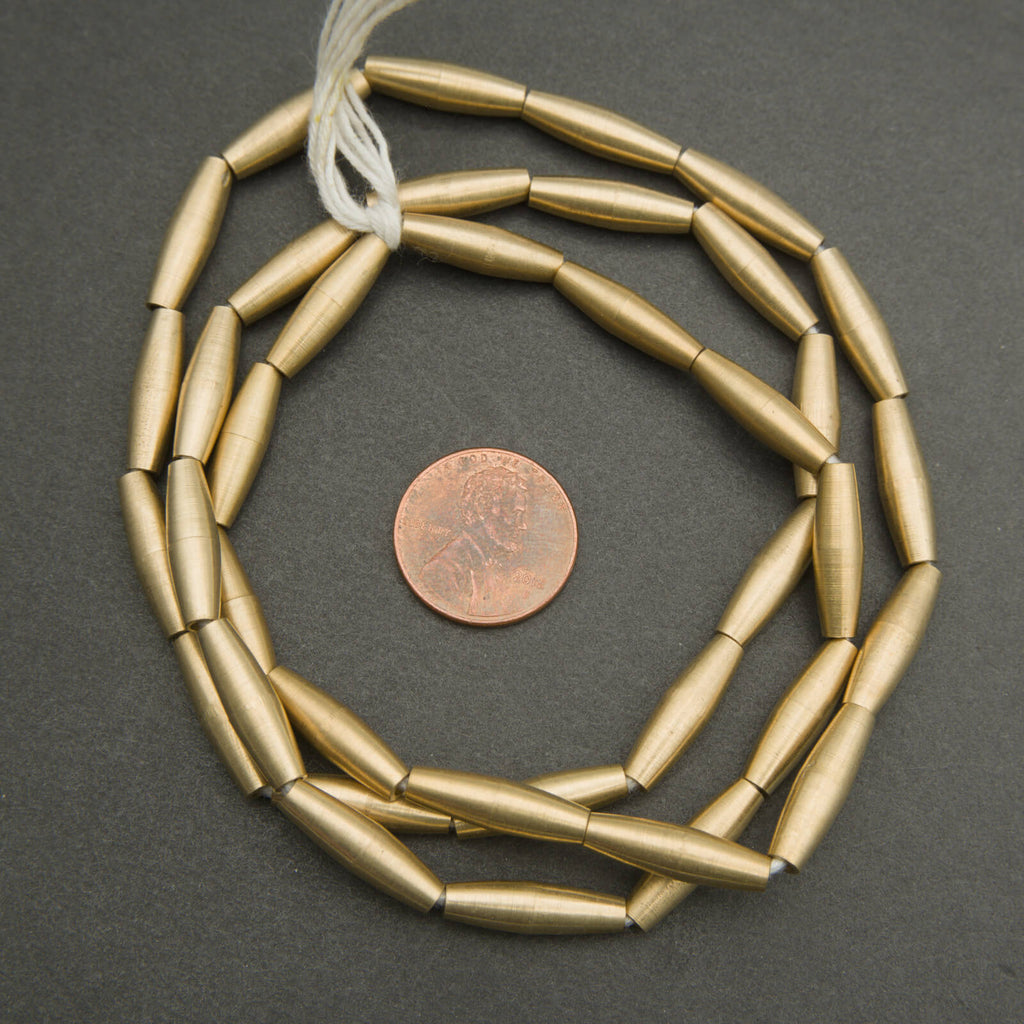 Gold beads on a string with a penny for scale on a gray background