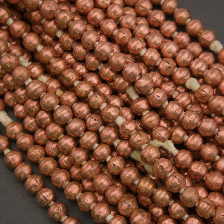 Multiple strands of metallic copper-colored round beads threaded on white cord, photographed close-up against a dark gray background.