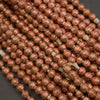 Multiple strands of metallic copper-colored round beads threaded on white cord, photographed close-up against a dark gray background.