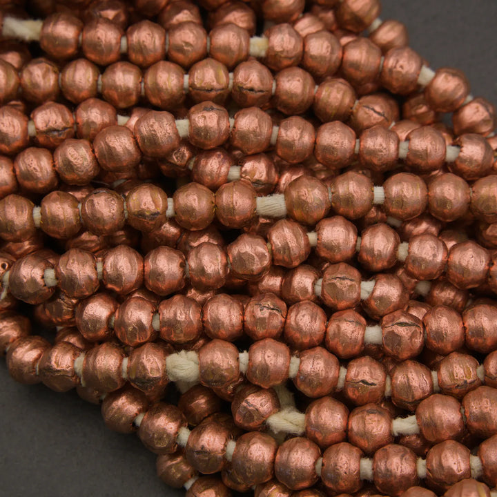 A close-up of copper-colored seed beads threaded on white cord, piled together on a dark gray background.