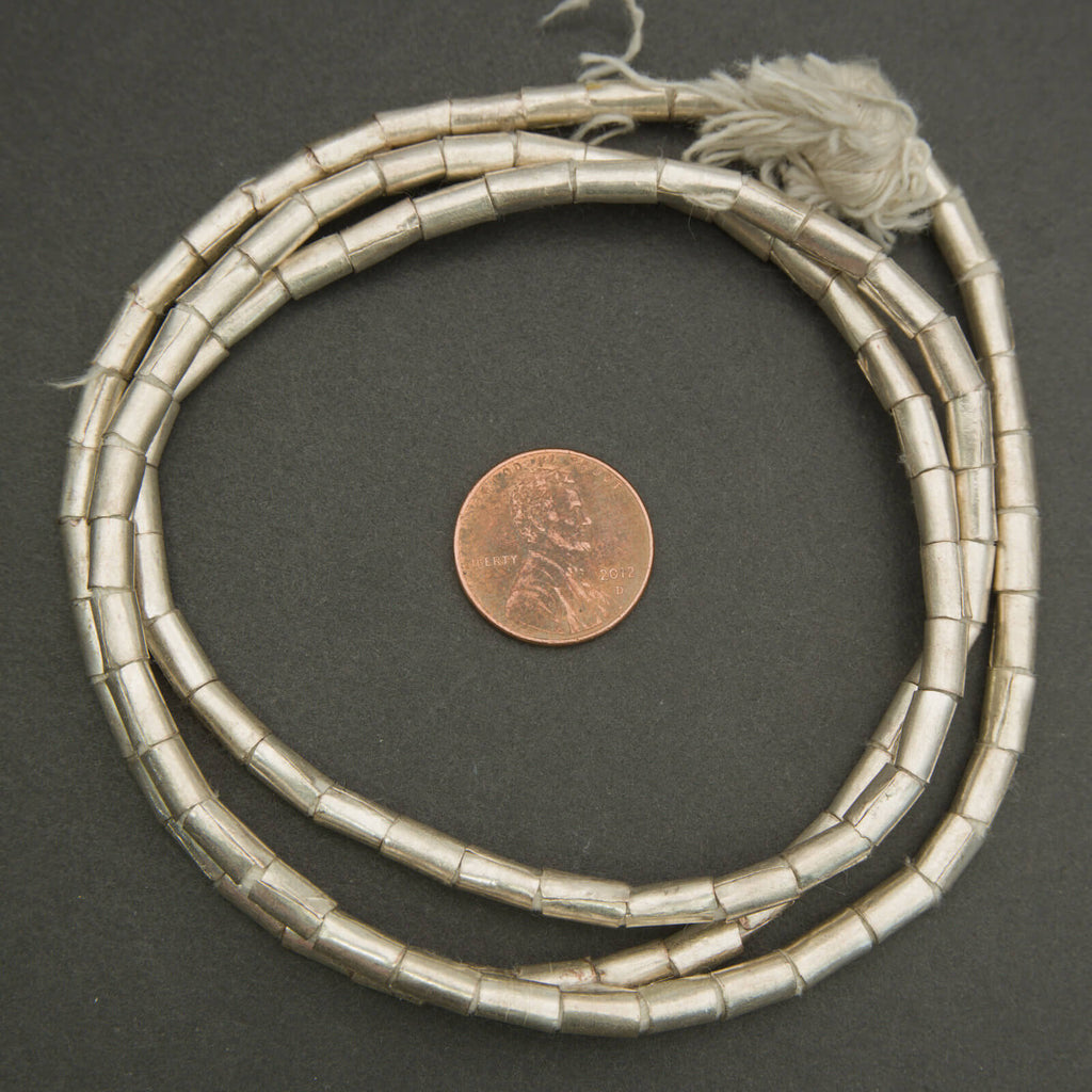 Silver beaded necklace with tassel on a dark surface, next to a penny for scale.