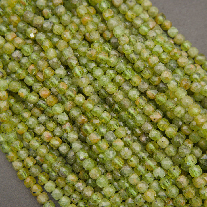 Faceted round beads in a light olive green color with subtle yellowish-orange and white marbling, arranged in diagonal rows on a neutral gray background.