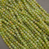 Faceted round beads in a light olive green color with subtle yellowish-orange and white marbling, arranged in diagonal rows on a neutral gray background.