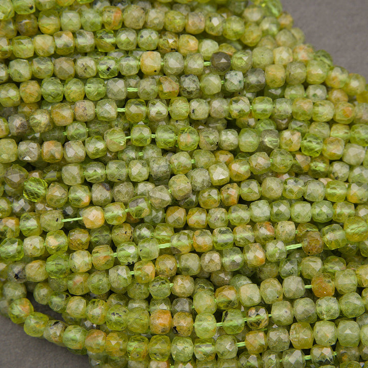 Faceted round beads strung on a cord, showing a marbled mix of olive green, yellow, and orange-brown tones, photographed close-up on a neutral gray surface.