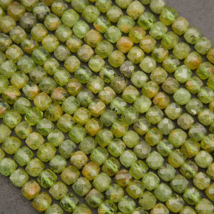 Faceted round beads in a light olive green color with natural yellow and orange-brown inclusions, arranged in diagonal rows on a dark gray background.
