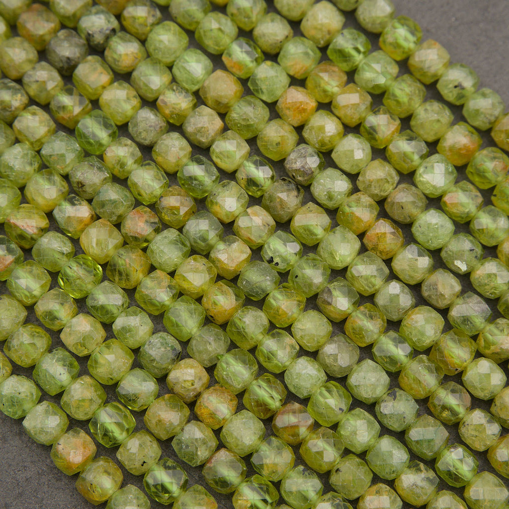 Faceted round beads in a light olive green color with natural yellow and orange-brown inclusions, arranged in diagonal rows on a dark gray background.