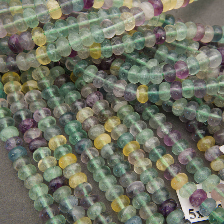 Close-up of polished fluorite rondelle beads displaying transparent to cloudy surfaces and varied colors.