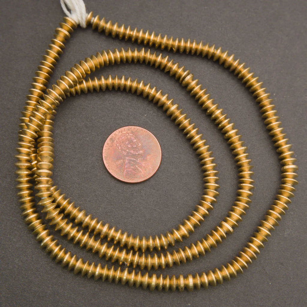 Gold spiral necklace with a penny for scale on a gray background