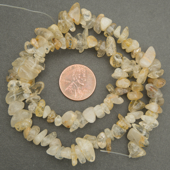 Necklace of small, irregularly shaped stones on a gray background with a penny for scale.