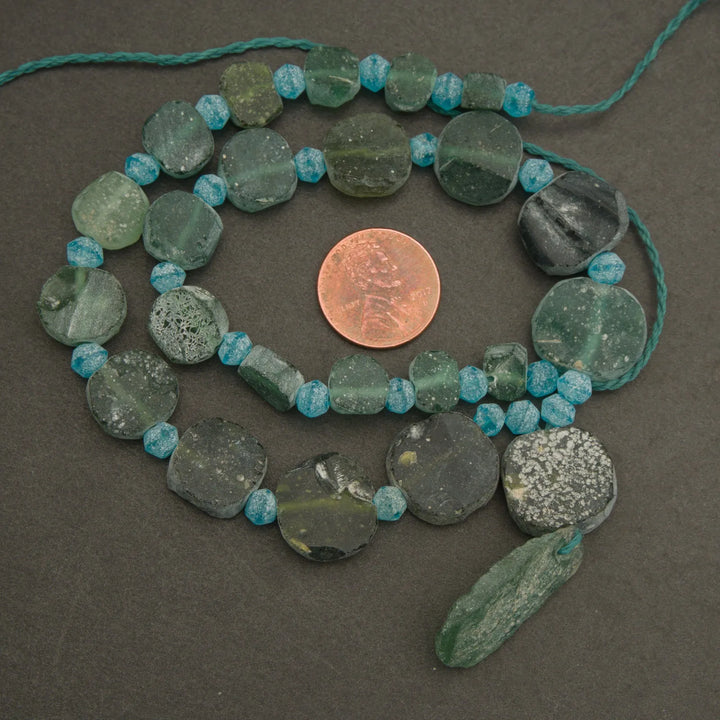 Necklace with green and blue beads on a dark surface, with a penny for scale.