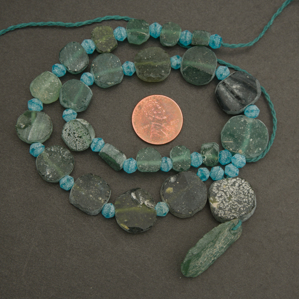 Necklace with green and blue beads on a dark surface, with a penny for scale.