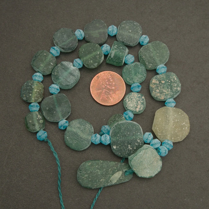 Necklace with green and blue beads on a dark surface, with a penny for scale.
