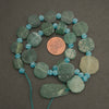Necklace with green and blue beads on a dark surface, with a penny for scale.