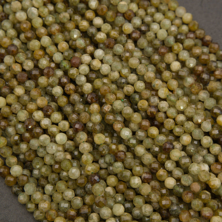 A close-up pile of small faceted round beads in earthy olive green, tan, brown, and cream tones on a dark gray background.
