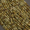A close-up pile of small faceted round beads in earthy olive green, tan, brown, and cream tones on a dark gray background.