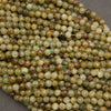 A close-up pile of faceted round beads in earthy olive green, tan, brown, and cream tones, strung on thin green cords against a dark gray background.