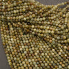 A close-up pile of small faceted round beads in earthy olive green, tan, brown, and cream tones on a dark gray background.
