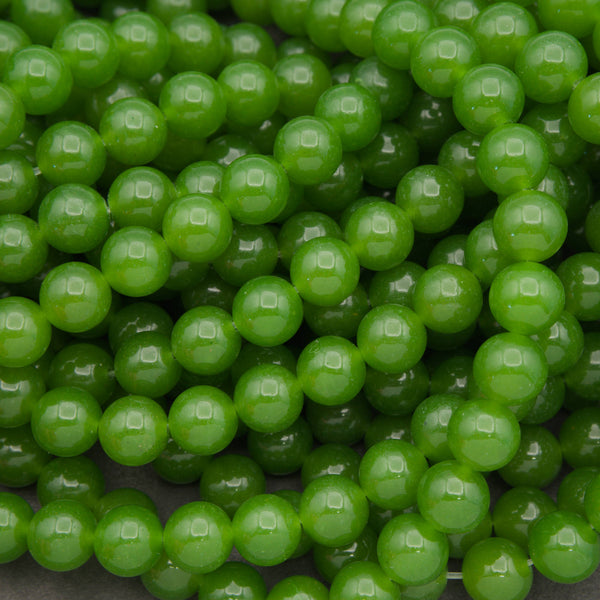 A close-up pile of glossy, round green beads with a smooth, polished surface.
