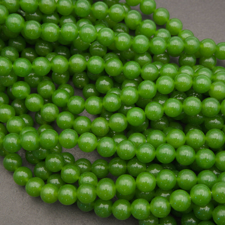 Green round gemstone beads arranged in overlapping strands on a neutral gray background.