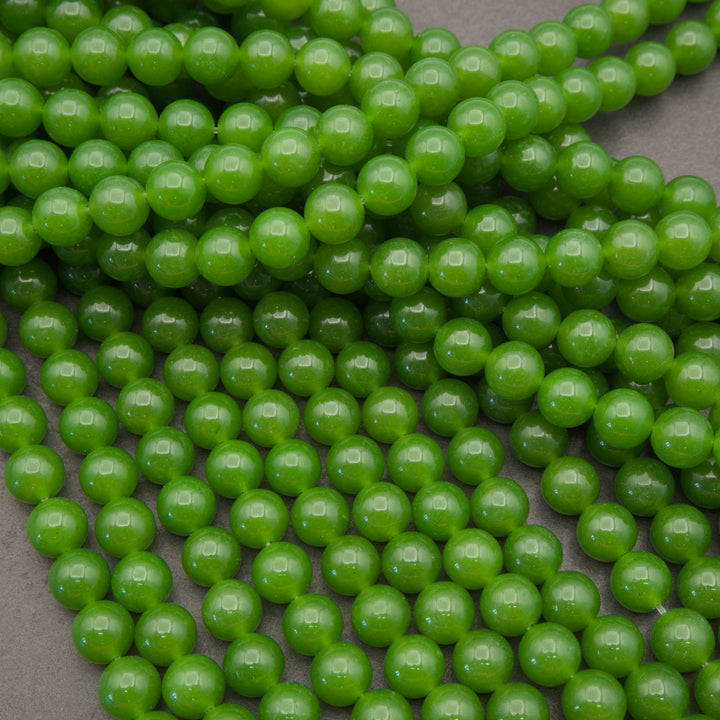 Green round glass beads with a glossy finish, arranged in overlapping strands on a neutral gray background.
