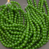 Multiple strands of glossy, translucent green round beads coiled together on a neutral gray background.
