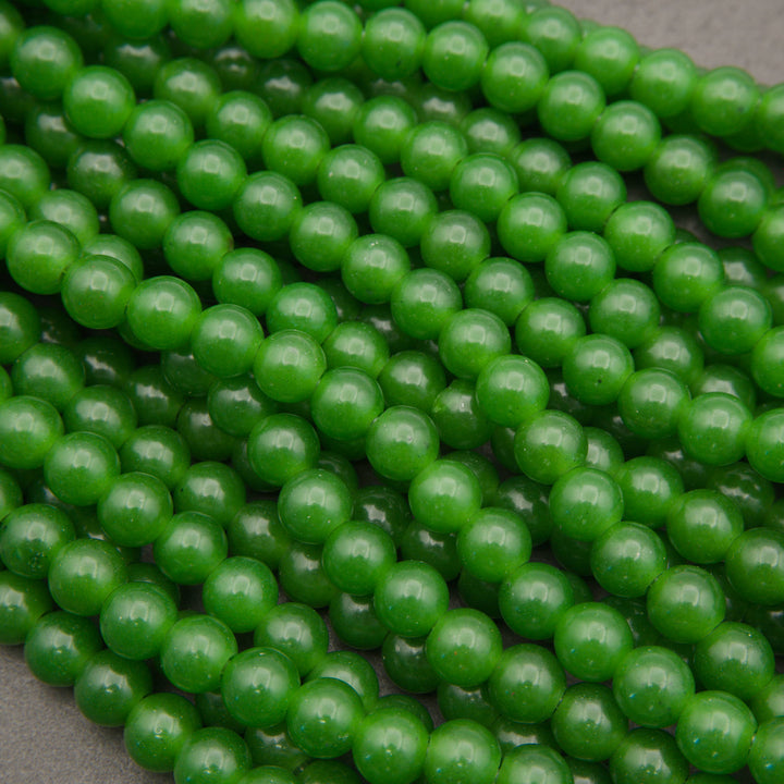 Rows of smooth round green jade large hole beads in deep green on a gray background