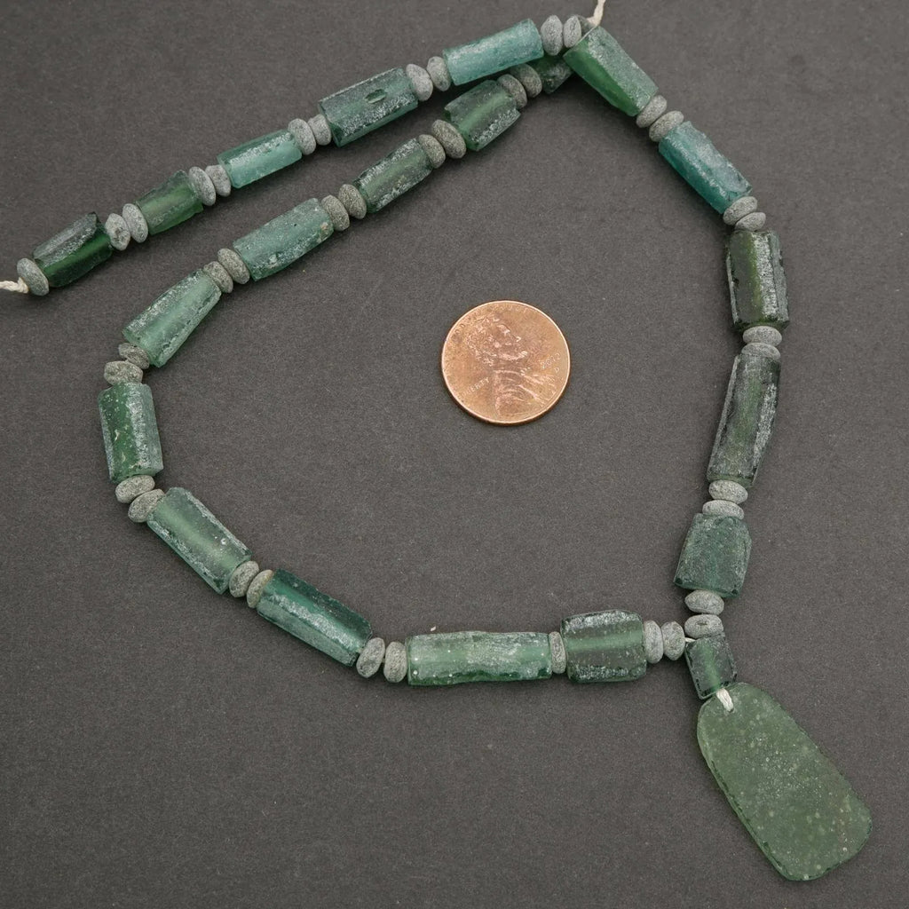 Green glass beads necklace with a penny for scale on a gray background