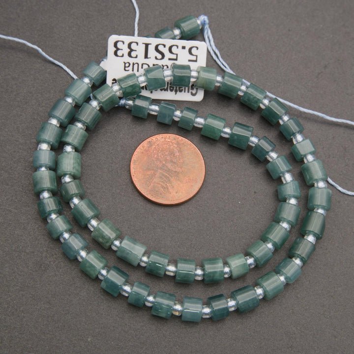 Green beaded necklace with a penny for scale on a gray background
