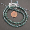 Green beaded necklace with a penny for scale on a gray background