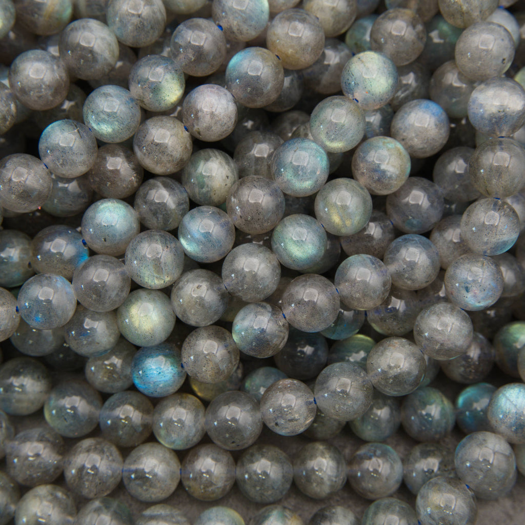 A close-up pile of polished round labradorite beads with a gray base and iridescent blue-green flashes.