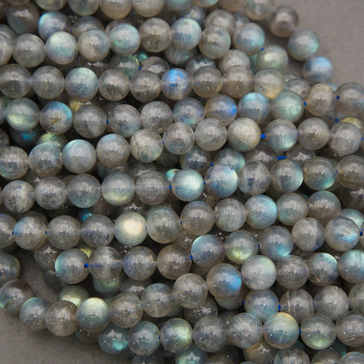 A pile of round labradorite beads with a gray base and a shimmering blue, green, and gold iridescent finish.