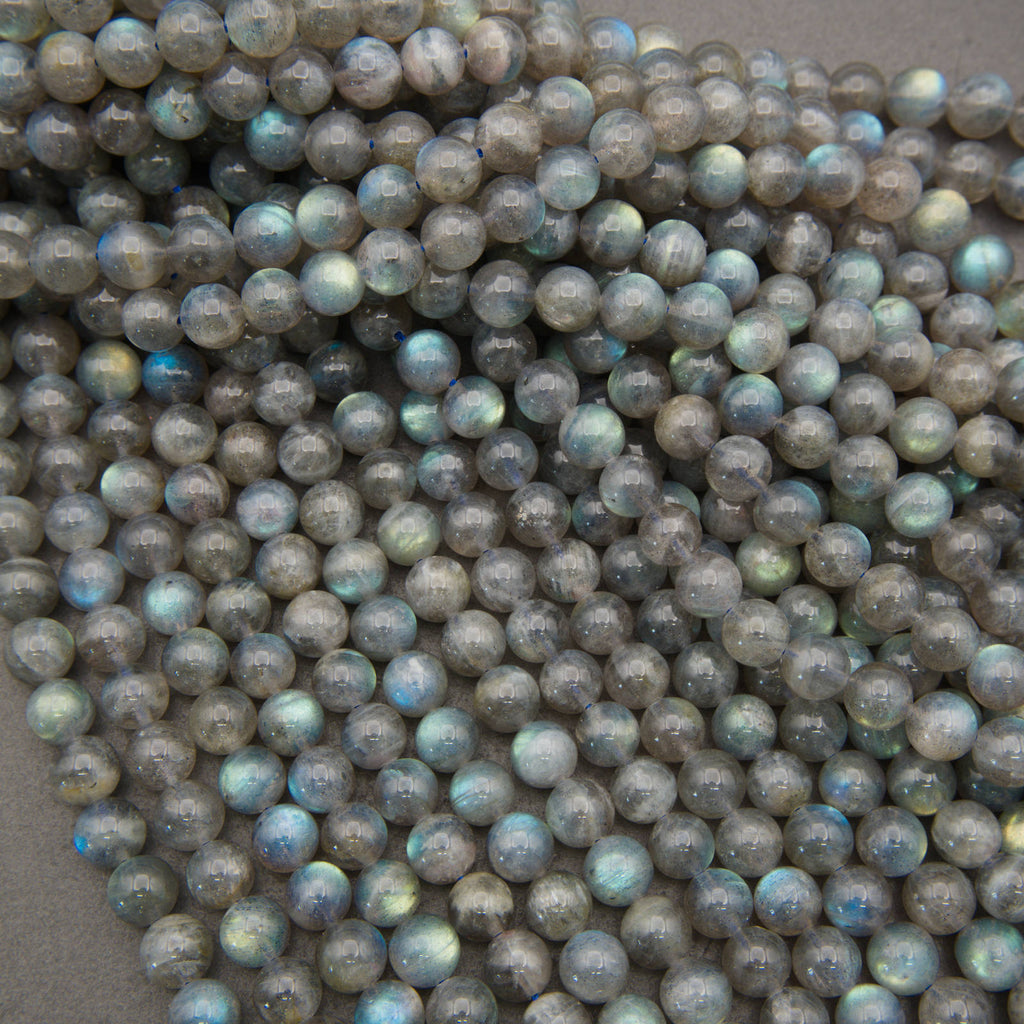 A pile of small, round, faceted beads made from labradorite stone, showing a characteristic gray base color with iridescent flashes of blue, green, and gold.