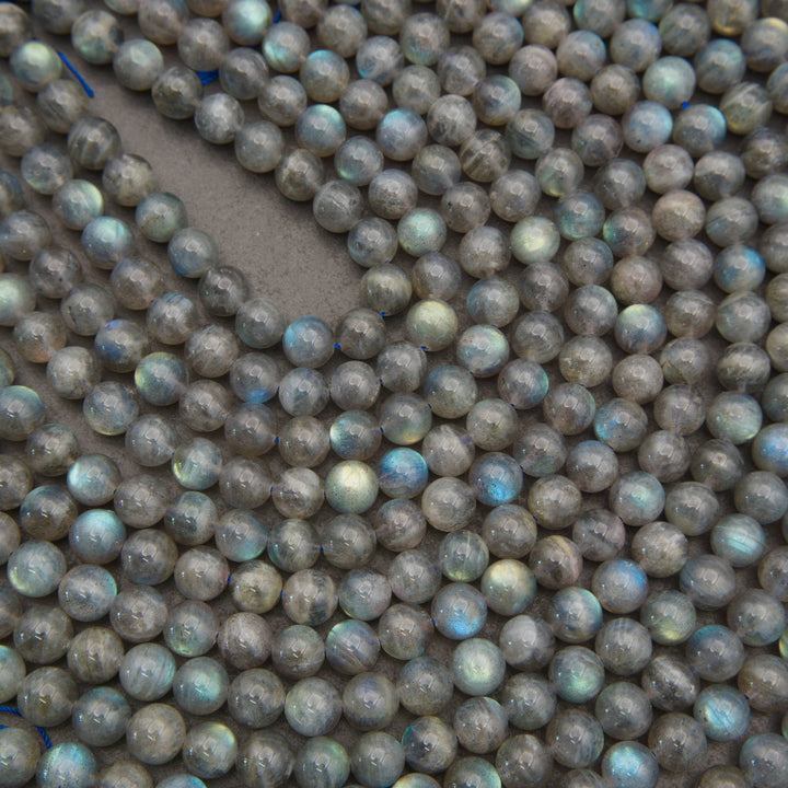 A close-up pile of round labradorite beads with a gray base and iridescent blue-green flashes.