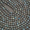 A close-up pile of round labradorite beads with a gray base and iridescent blue-green flashes.