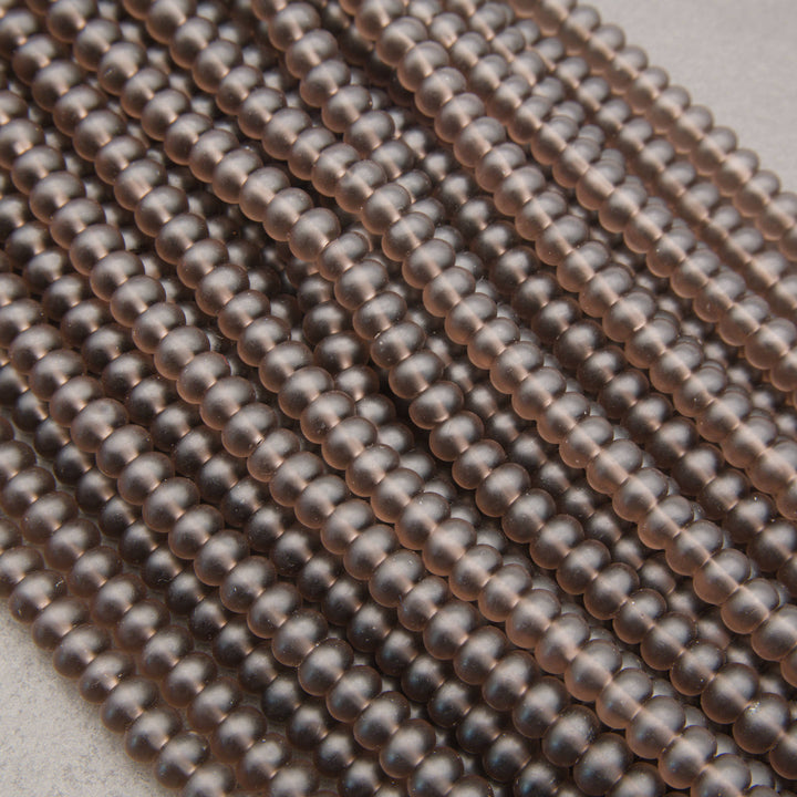 Close-up of multiple strands of small, round, metallic bronze beads arranged diagonally on a light neutral background.