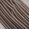 Close-up of multiple strands of small, round, metallic bronze beads arranged diagonally on a light neutral background.