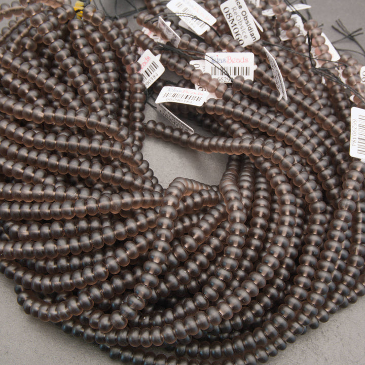 A large coil of dark brown translucent faceted beads with small white product tags attached, photographed on a neutral gray surface.