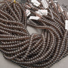 A large coil of dark brown translucent faceted beads with small white product tags attached, photographed on a neutral gray surface.