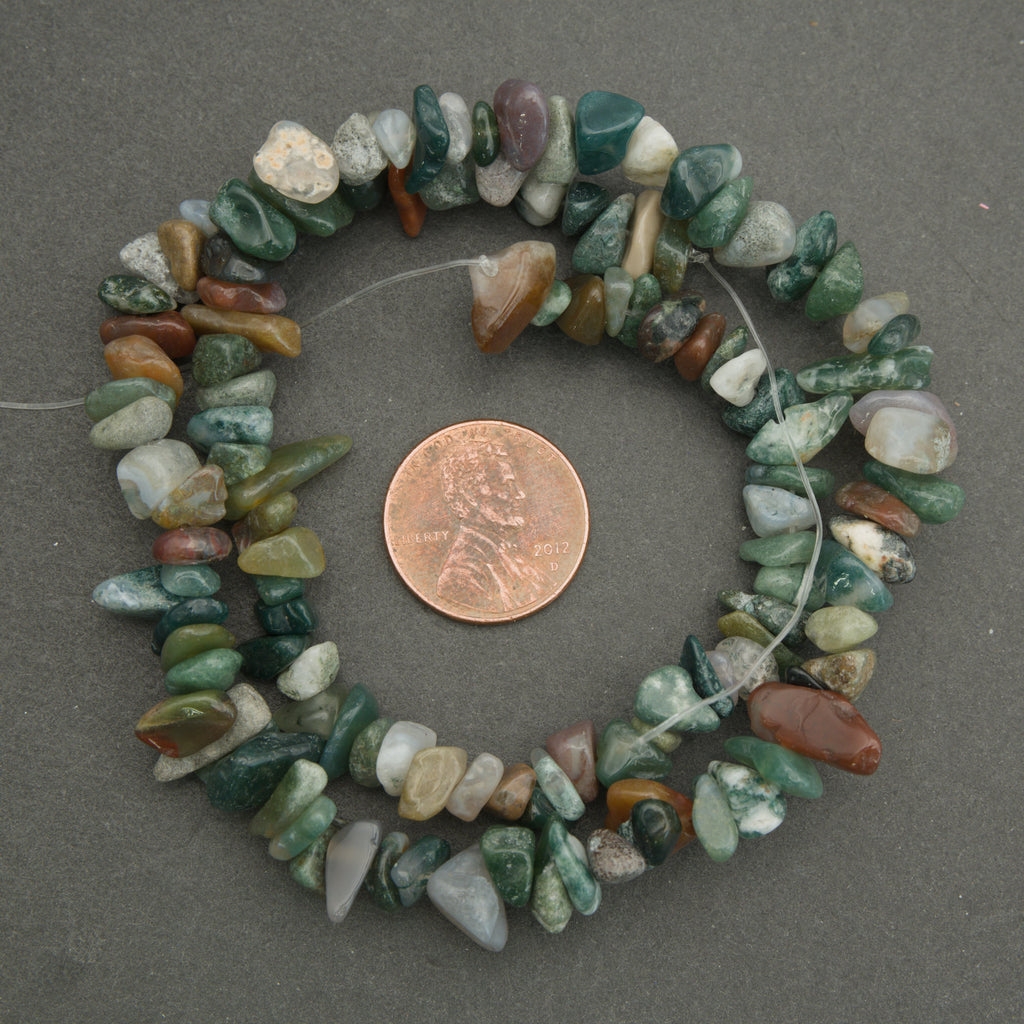 Necklace of multicolored stones with a penny for scale on a gray background