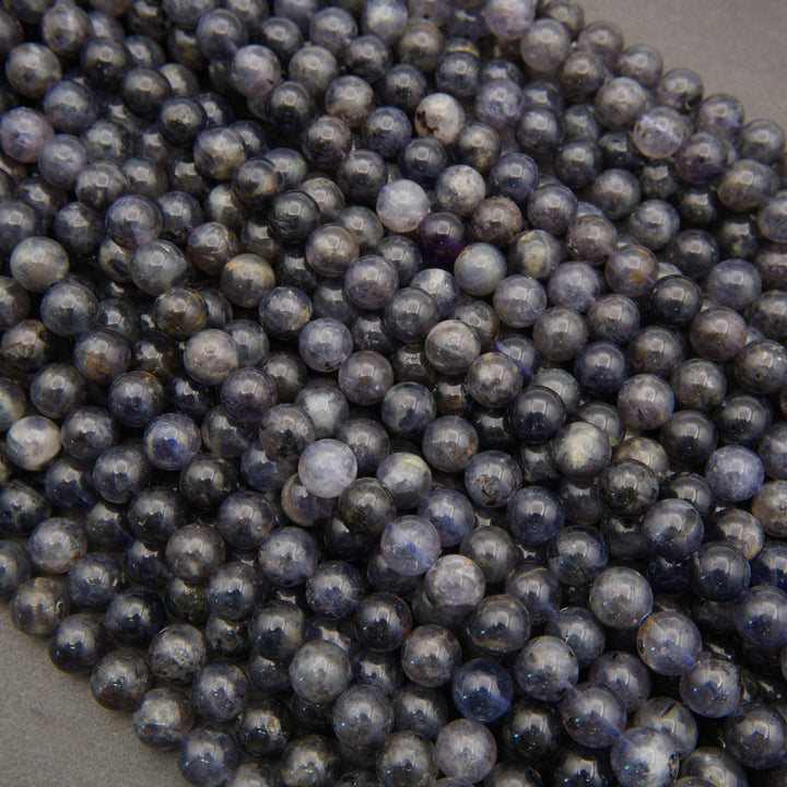 Close-up of iolite round beads with glossy surfaces and varied shades of violet-blue and slate gray.