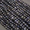 Close-up of iolite round beads with glossy surfaces and varied shades of violet-blue and slate gray.