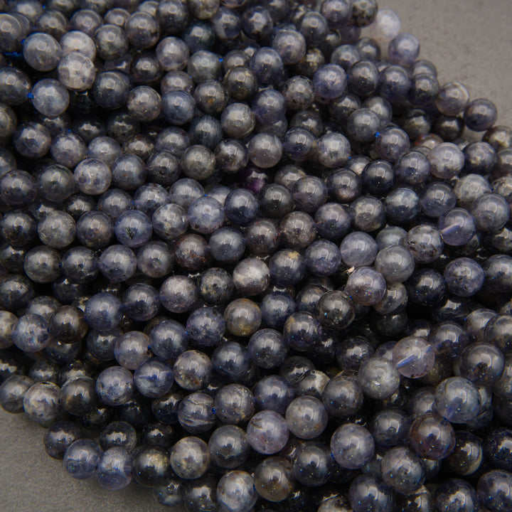 Strands of polished iolite beads featuring dark sapphire-blue hues and natural mineral variations.