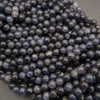 Strands of polished iolite beads featuring dark sapphire-blue hues and natural mineral variations.