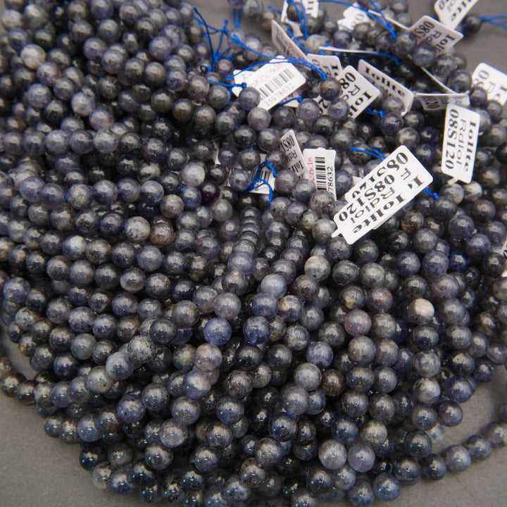 Smooth iolite round beads in shades of indigo, lavender-gray, and smoky blue with natural mottled patterns.