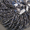 Smooth iolite round beads in shades of indigo, lavender-gray, and smoky blue with natural mottled patterns.