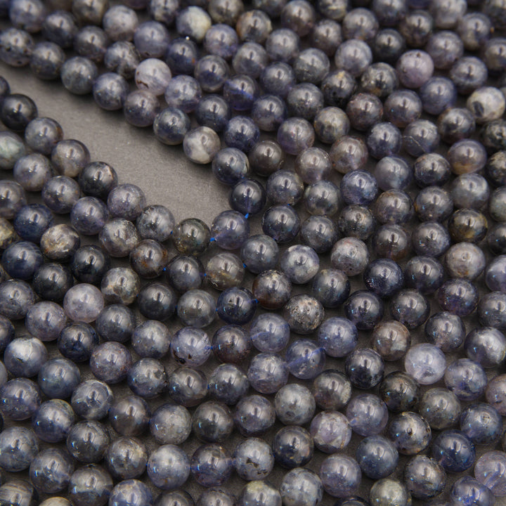 Polished iolite round beads featuring deep indigo, smoky violet, and natural gray mineral inclusions.