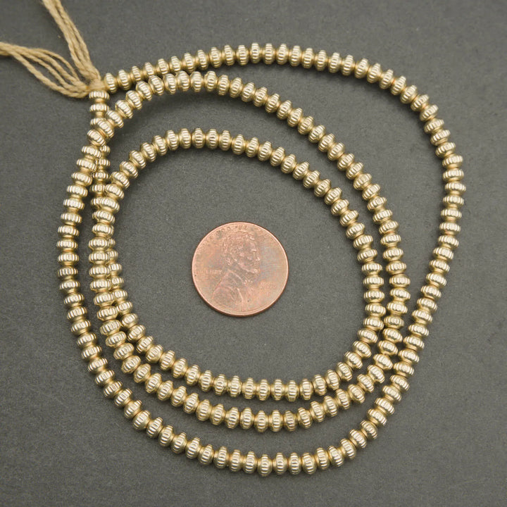 Gold beaded necklace on a dark surface with a penny for scale
