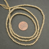 Gold beaded necklace on a dark surface with a penny for scale