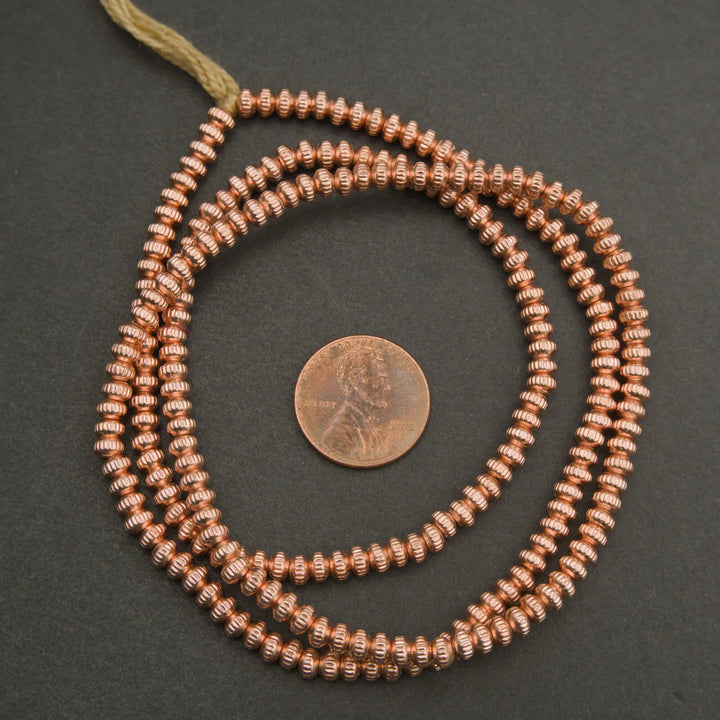 Copper beaded necklace with a penny for scale on a dark background
